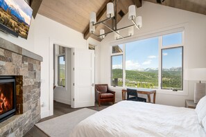 Relax in this serene bedroom with a large bed, stone fireplace, and breathtaking mountain views.