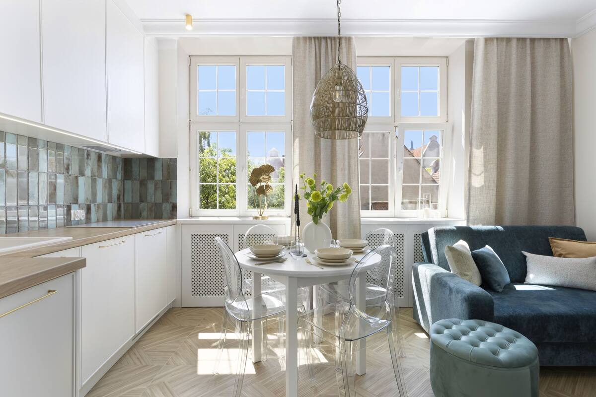 A modern kitchen with white cabinets, a dining table with clear chairs, and a blue sofa.