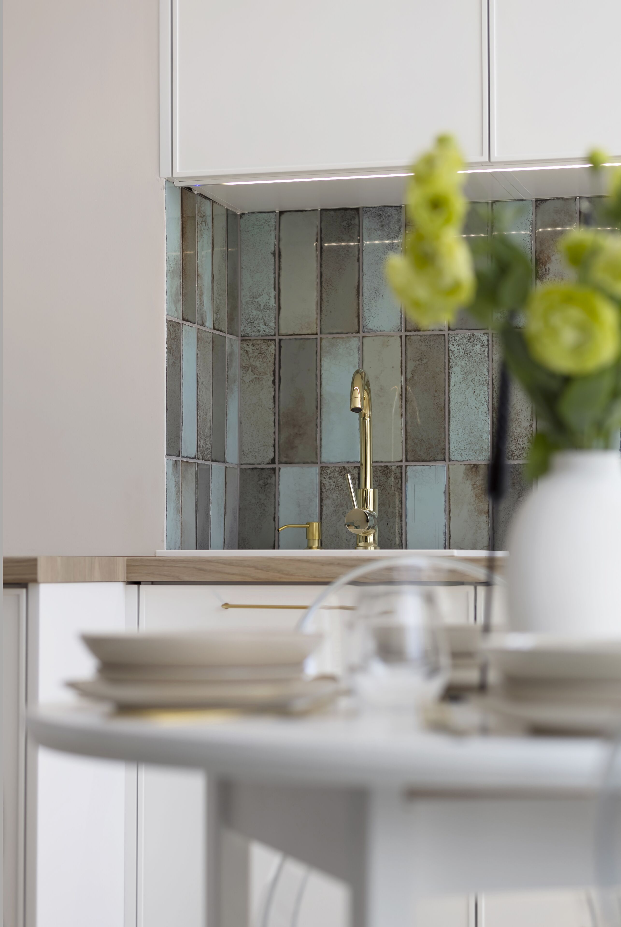 Een moderne keuken met een betegelde spatwand, een gouden kraan en een vaas met bloemen op het aanrecht.