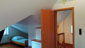 A bedroom with a sloped ceiling, a bed, a wooden door, and a staircase leading to another room.