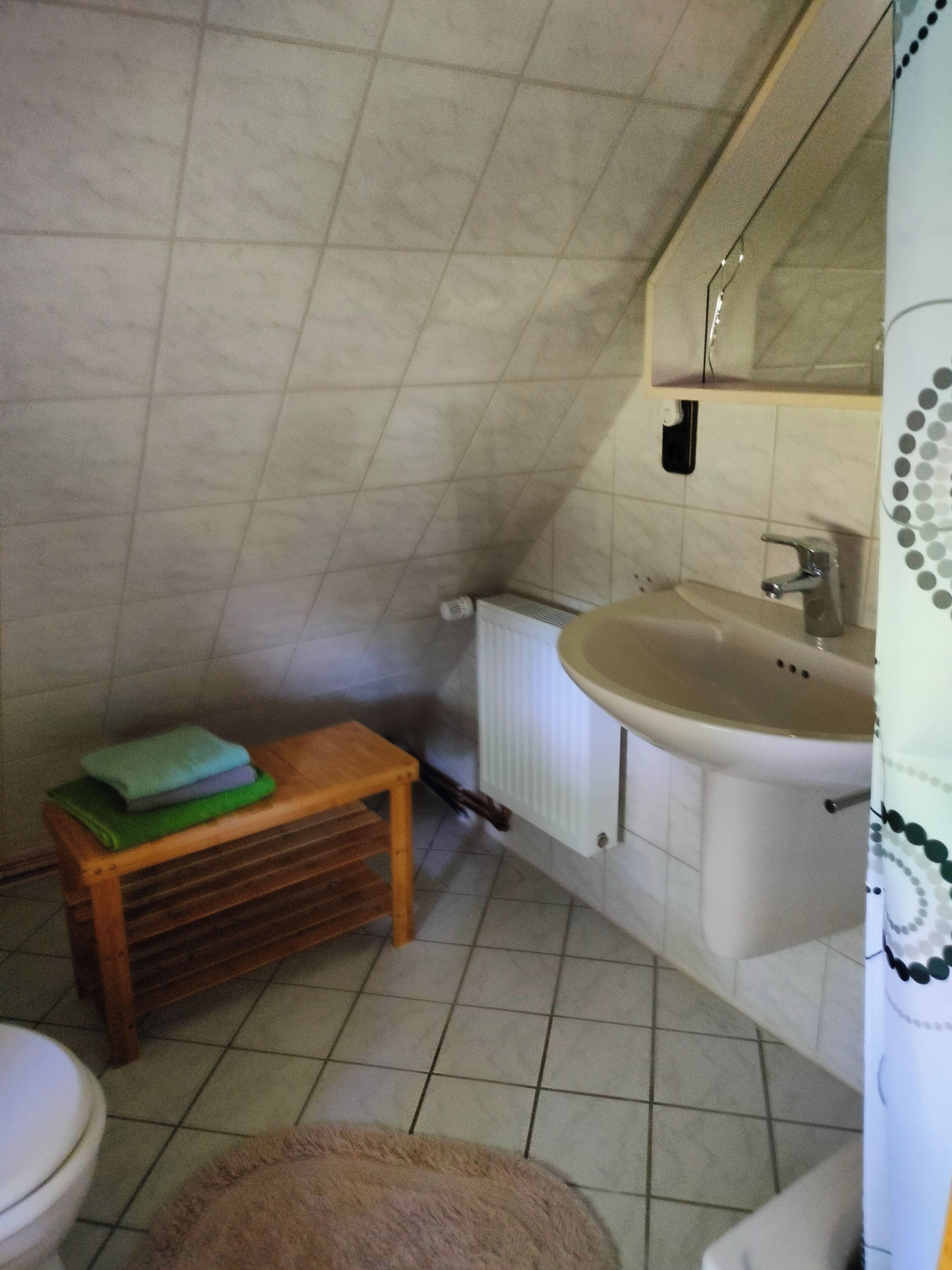Une petite salle de bain avec des toilettes, un lavabo et un tabouret en bois sur lequel sont pliées des serviettes.