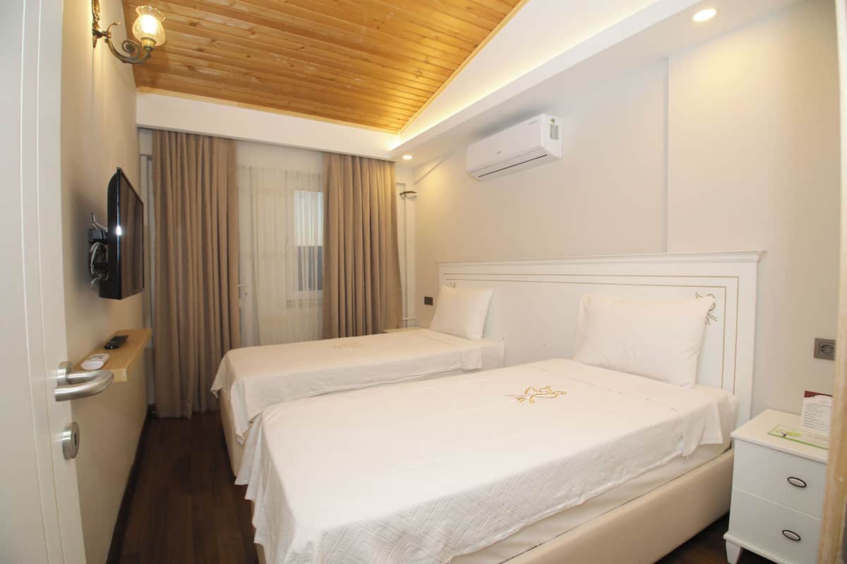 A hotel room with two beds, a wooden ceiling, an air conditioning unit, a TV, and a bedside table with a lamp.