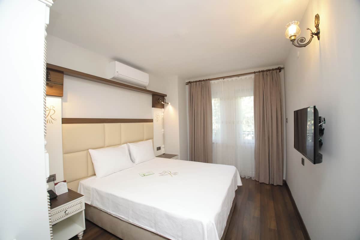 A hotel room with a bed, a nightstand, a TV, and a wall-mounted light fixture.