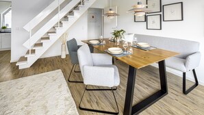 Ein moderner Essbereich mit einem Holztisch, grau gepolsterten Stühlen und einer weißen Treppe.