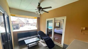 A hotel room with a bed, a small table, a sofa, a ceiling fan, and a sliding glass door leading to a balcony. - The Sports Lounge (Pattaya)