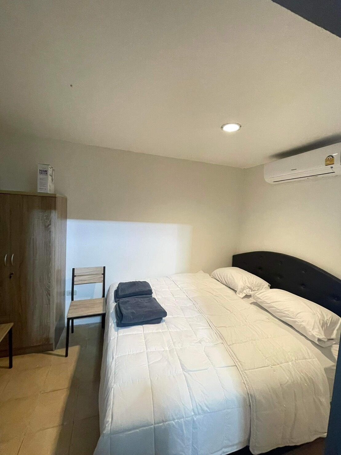 Un dormitorio con cama, una silla, un armario y un equipo de aire acondicionado.