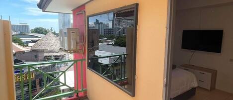 Uma varanda com piso de azulejos, uma cama com televisão e vista para prédios e uma ponte.