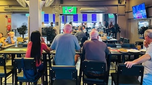 A restaurant with multiple tables and chairs, ceiling fans, and a television screen. - The Sports Lounge (Pattaya)
