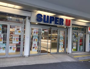 Loja Super U com portas de vidro e vários cartazes promocionais.