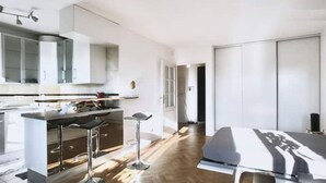 A modern kitchen with a bar area, a dining table, and a large wardrobe. - Appartement Paris (Paris)