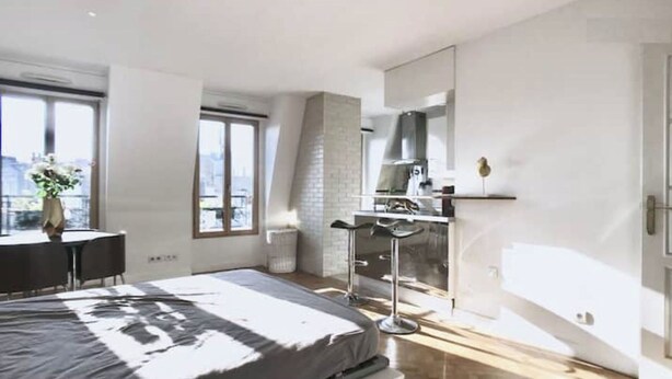 A modern bedroom with a large bed, a desk, and a balcony with a city view. - Appartement Paris (Paris)