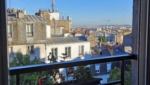 A balcony with a bicycle, overlooking a cityscape with various buildings and clear skies. - Appartement Paris (Paris)