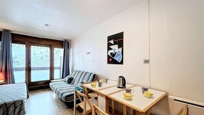 A cozy room with a bed, a sofa, a dining table with chairs, and a window with curtains.