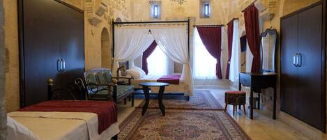 Una cama con dosel, una mesita redonda pequeña y una silla en una habitación con paredes de piedra y un candelabro.