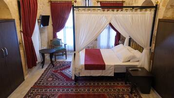 A traditional room with a four-poster bed, red and white drapes, a patterned carpet, and stone walls.