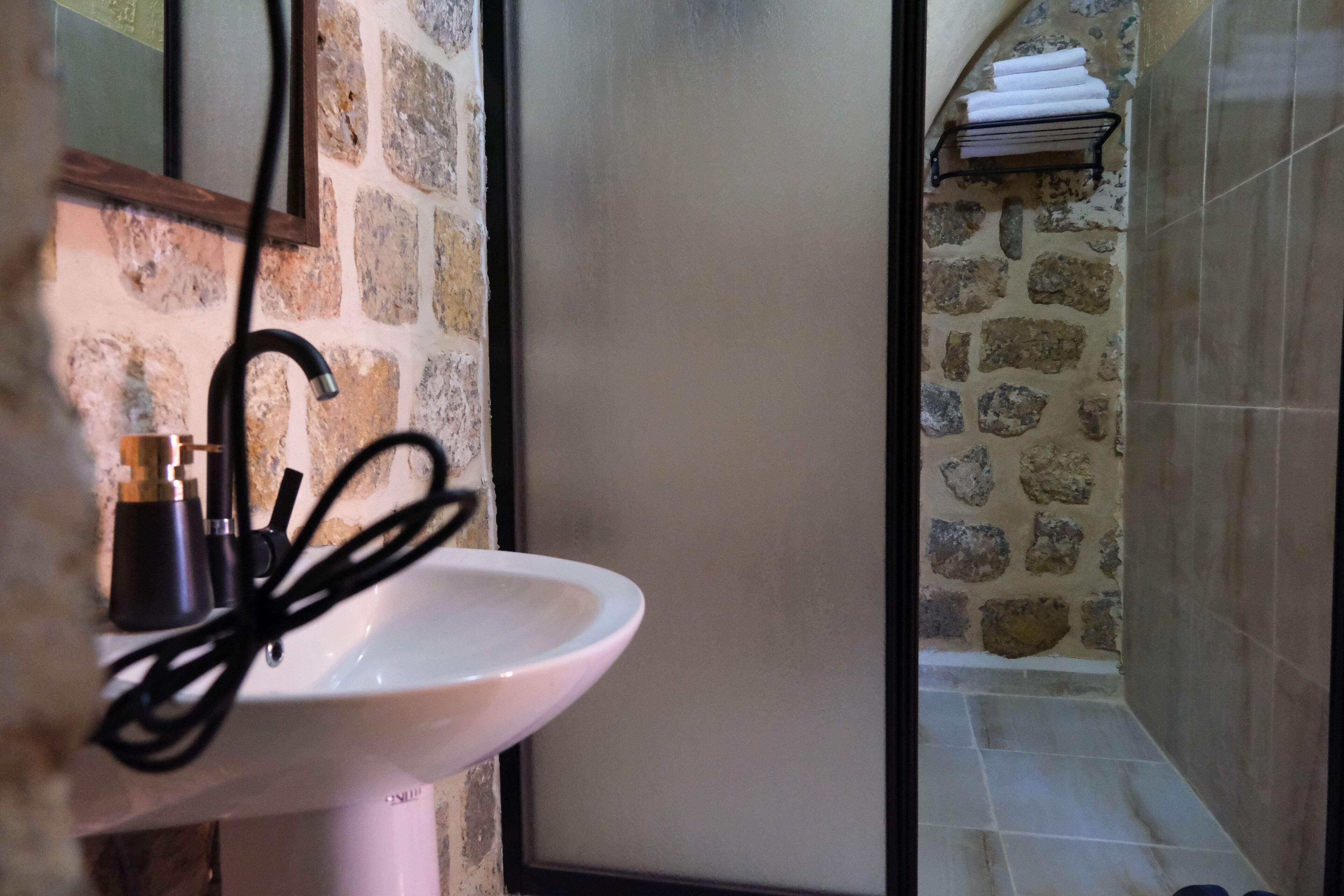 Un baño con pared de piedra, lavamanos blanco y toallero.