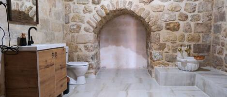 A bathroom with a stone archway, a wooden vanity, a white toilet, and a marble floor.