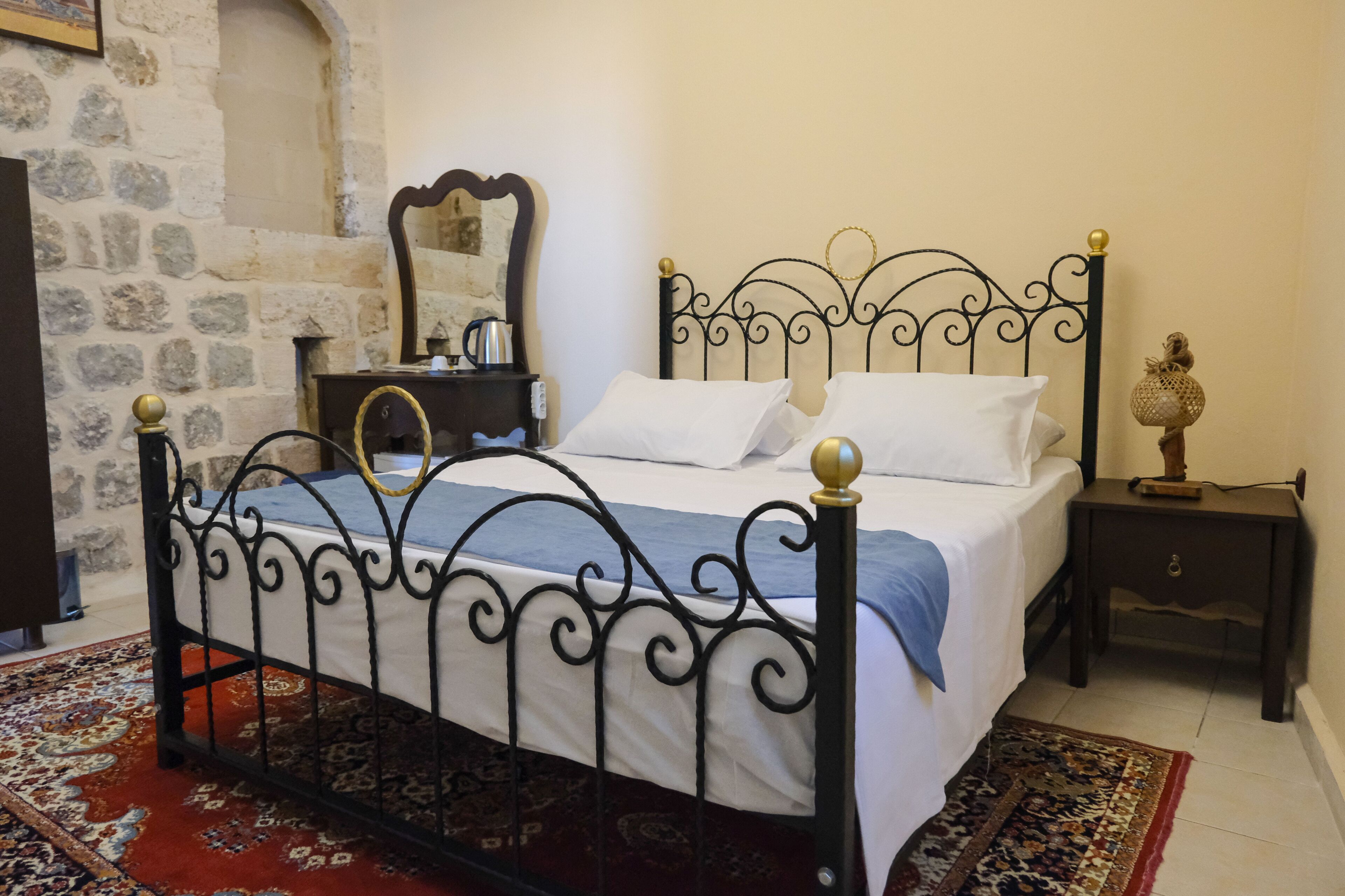 A room with a bed, a nightstand, a mirror, and a stone wall.