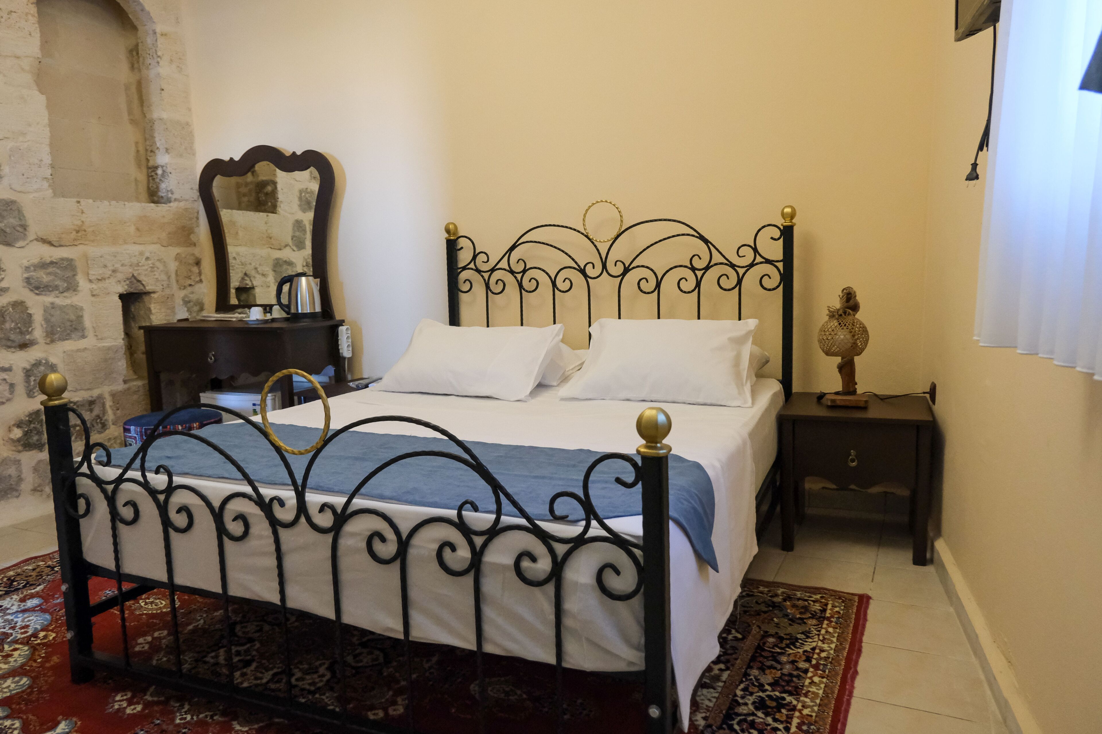 A bed with a metal frame, a bedside table, a nightstand, a mirror, and a patterned rug.