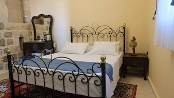 A bed with a metal frame, a bedside table, a nightstand, a mirror, and a patterned rug.