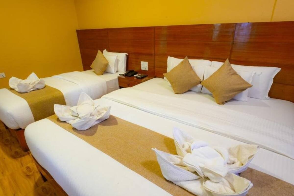 Une chambre d’hôtel avec deux lits, une tête de lit en bois, du linge de lit blanc et des serviettes disposées sur le sol.