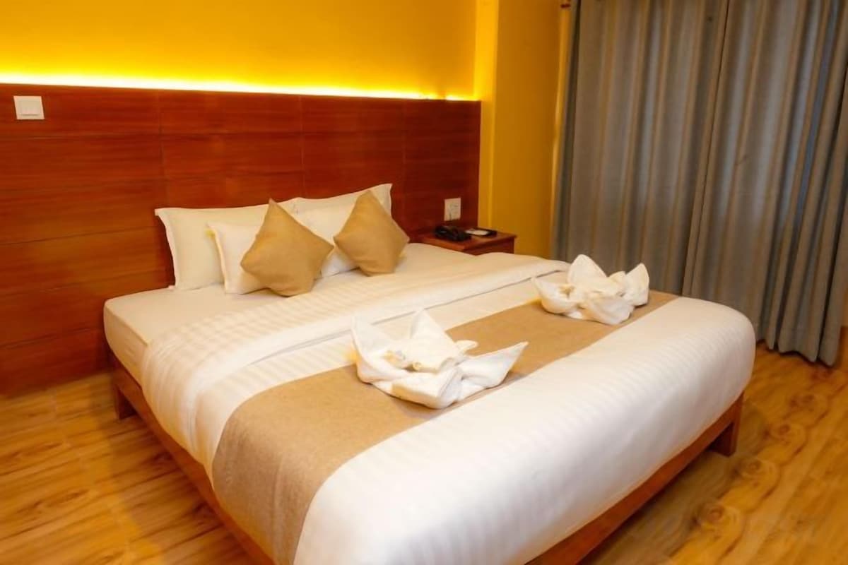 Een hotelkamer met een houten hoofdeinde, een net opgemaakt bed met witte lakens en een nachtkastje met een lamp.