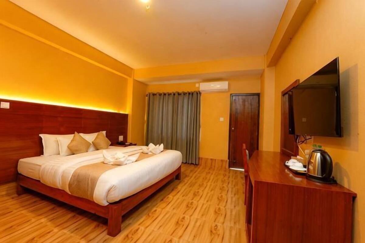Une chambre d’hôtel avec un lit en bois, un bureau, un téléviseur à écran plat et une fenêtre avec des rideaux.