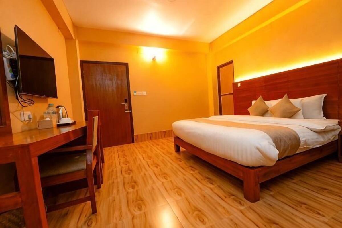 Une chambre d’hôtel avec un lit en bois, un bureau avec une chaise, une télévision et une porte.