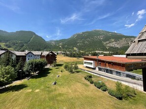 Un paysage montagneux parsemé de bâtiments, dont une construction moderne avec un toit rouge et un chalet traditionnel.