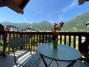 A balcony with a table and bench, overlooking a mountainous landscape.