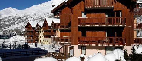 Un hotel in stile chalet di legno con diversi balconi e una montagna innevata sullo sfondo.