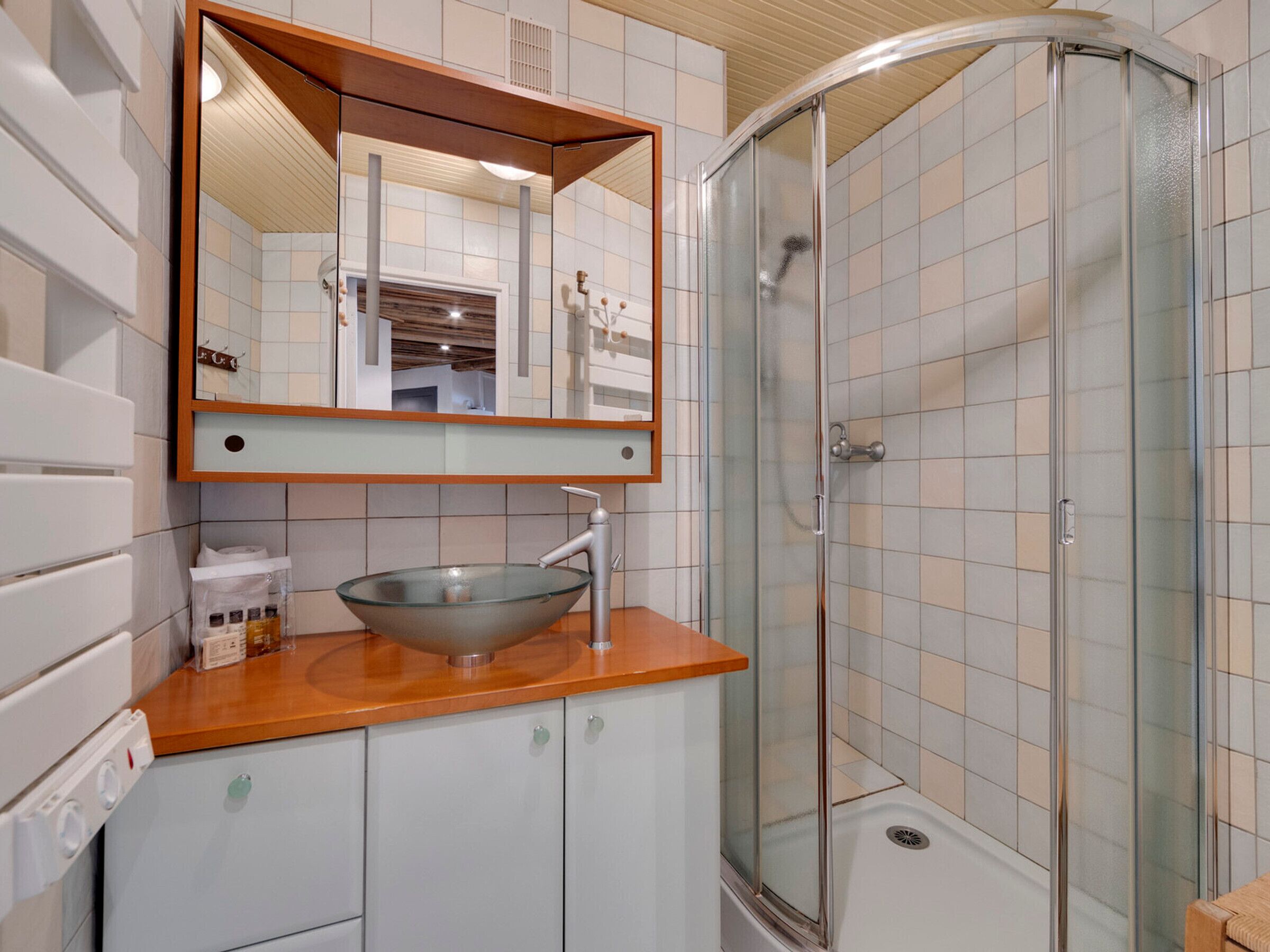 A bathroom with a glass-enclosed shower, a wooden vanity with a glass bowl sink, and a mirror above the sink.