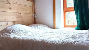 Una cama individual con un edredón blanco en una habitación con paredes de madera y una ventana con cortinas verdes.