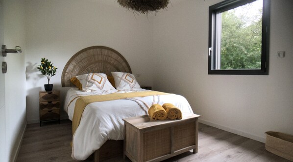 Un dormitorio con cama, mesitas de noche, una ventana y vistas a la vegetación.