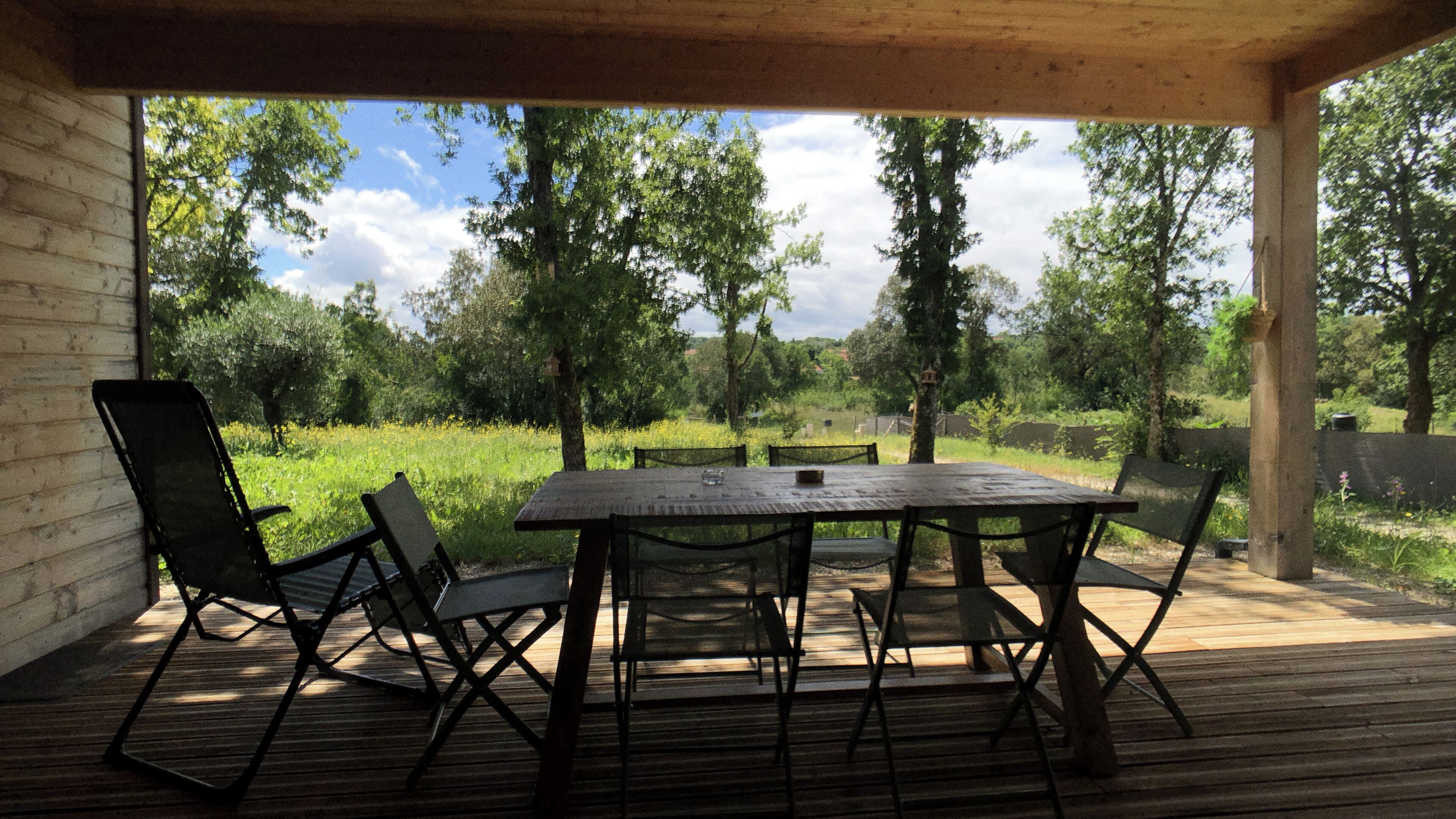 A wooden deck with a table and chairs, overlooking a grassy area with trees and a clear sky.