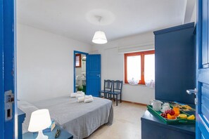 A bedroom with a bed, a desk with a lamp, a chair, a window with curtains, and a tray with fruits and a cup.