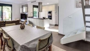 Une cuisine moderne avec des meubles blancs, un coin repas comprenant une table et des chaises, et un escalier menant à l’étage supérieur.