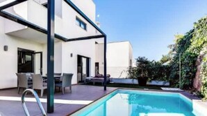 Un espace piscine extérieur moderne doté d’un patio couvert, d’un ensemble de mobilier de jardin et d’un petit jardin.
