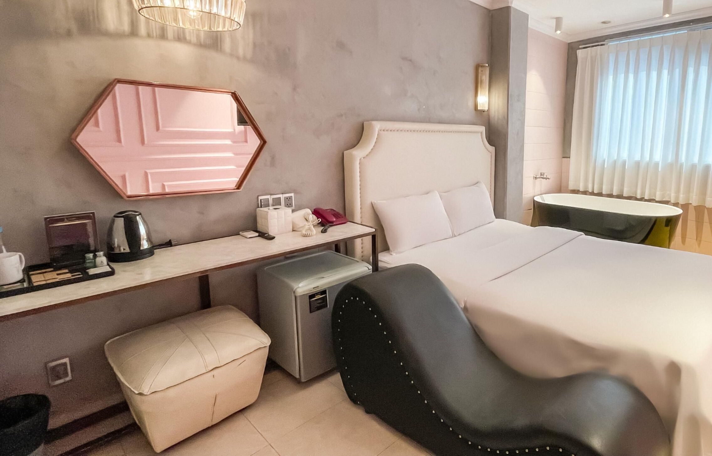A modern hotel room with a large bed, a desk with a computer, a chair, and a small table.