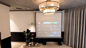 A modern living room with a large flat-screen TV mounted on a stand, a comfortable sofa, a small table with a plant, and a large window with curtains. - A IN HOTEL DEL LUNA (Ho Chi Minh City)