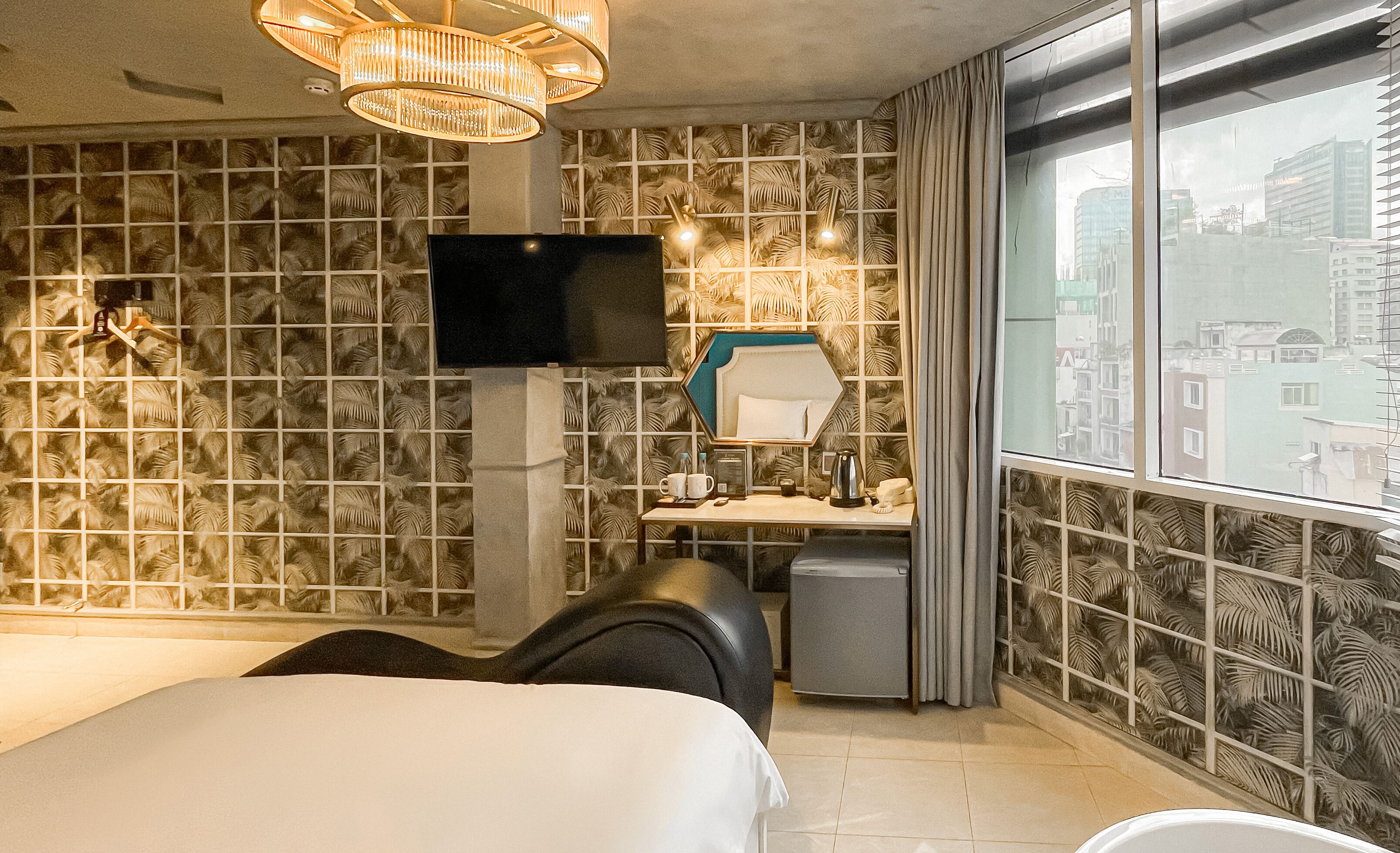A hotel room with a large bed, a desk with a chair, a television, and a view of the city through a large window.