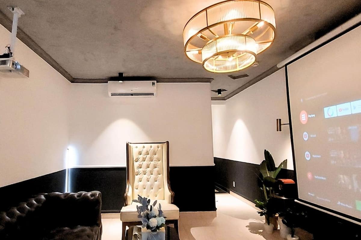 Un hall d’entrée moderne doté d’un écran de projection diffusant une présentation, d’un canapé moelleux, d’un lustre et d’un climatiseur fixé au mur.