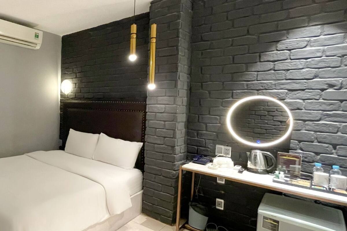 Une chambre d’hôtel avec un lit, un bureau doté d’un miroir et un mur en briques noires.