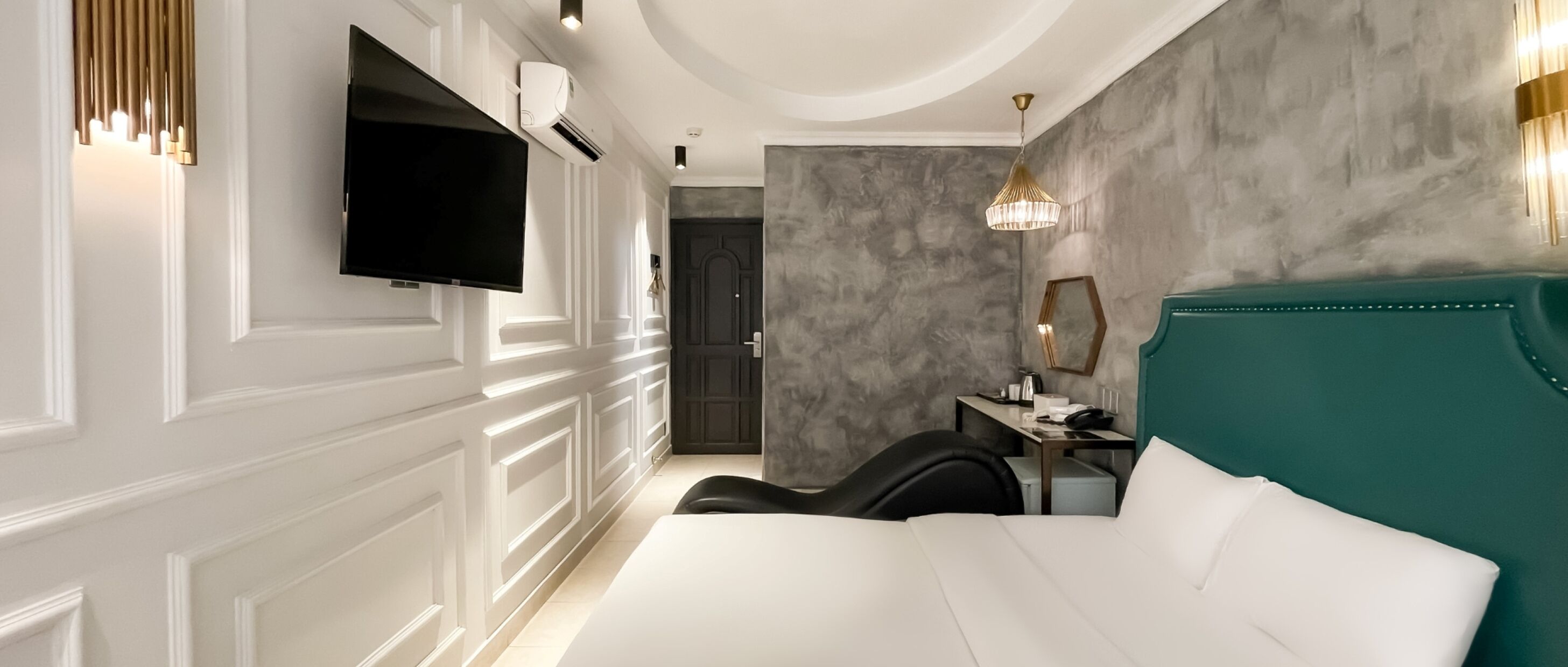 Una habitación de hotel moderna con una cama grande, un escritorio con silla, un televisor de pantalla plana y una araña.