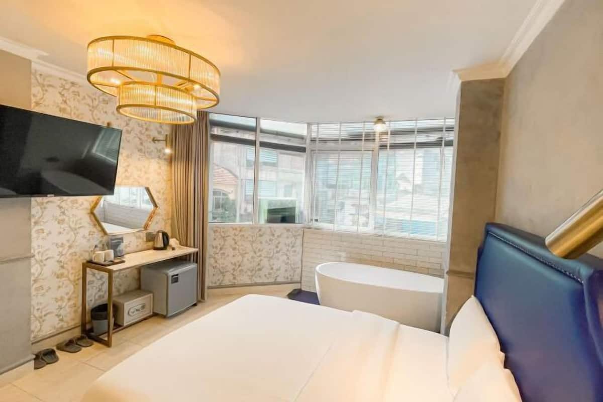 Une chambre d’hôtel avec un lit, un bureau, une télévision, une fenêtre et une baignoire.