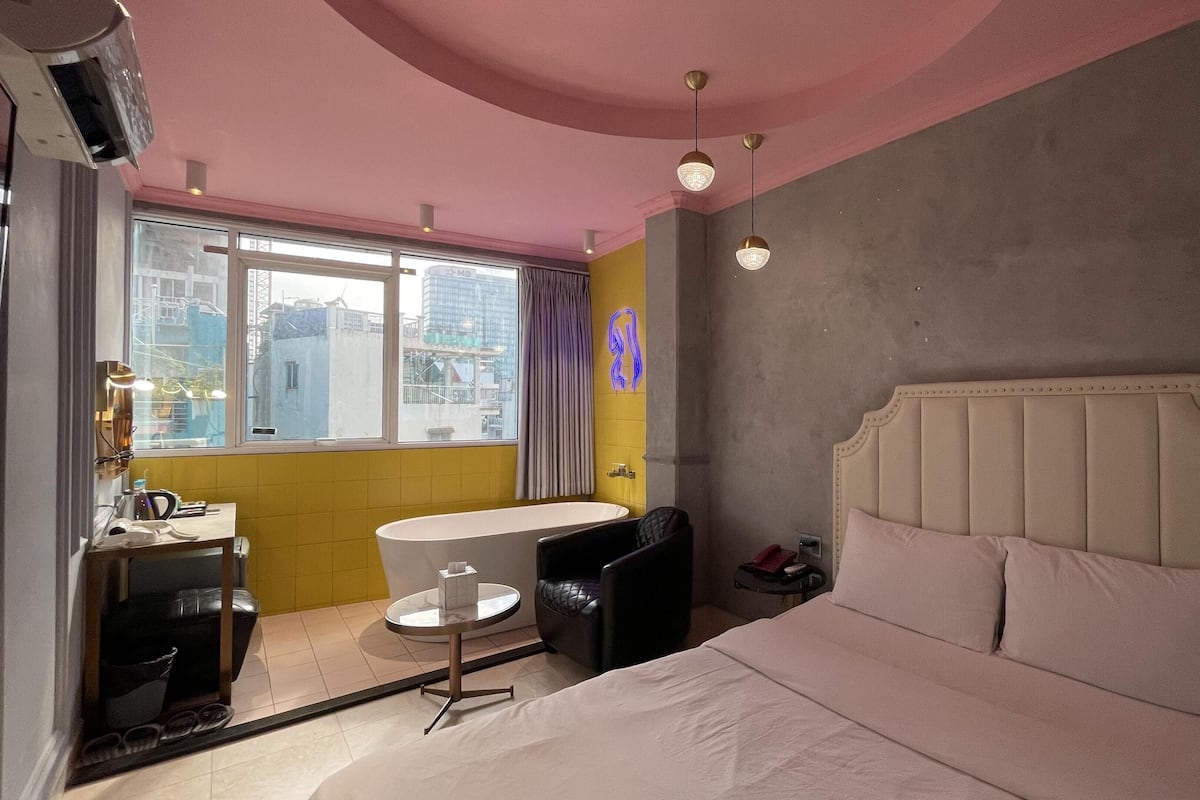 Une chambre d’hôtel avec un lit, une table ronde, une chaise, un petit bureau, une fenêtre et une vue sur la ville.