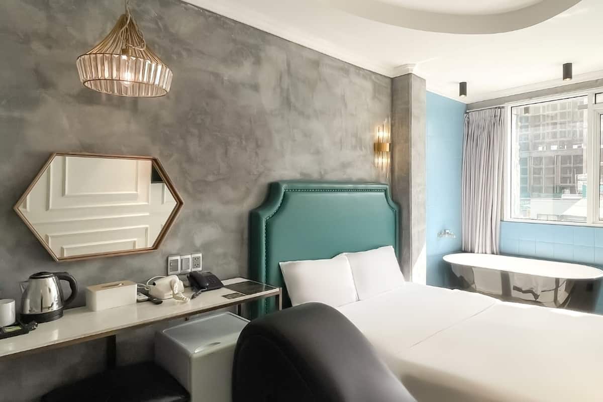 Une chambre d’hôtel avec un grand lit, un bureau avec un téléphone et une bouilloire, un miroir et une fenêtre donnant sur des immeubles.
