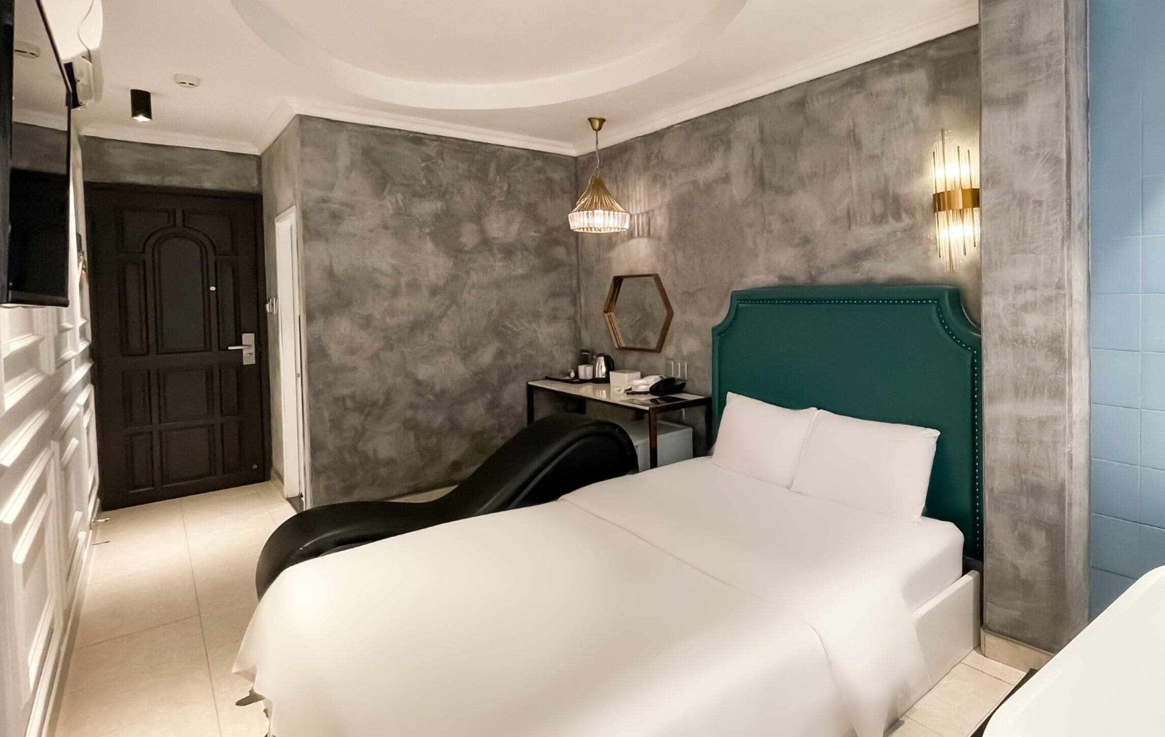 A modern hotel room with a large bed, a desk, a chair, and a mirror on the wall.