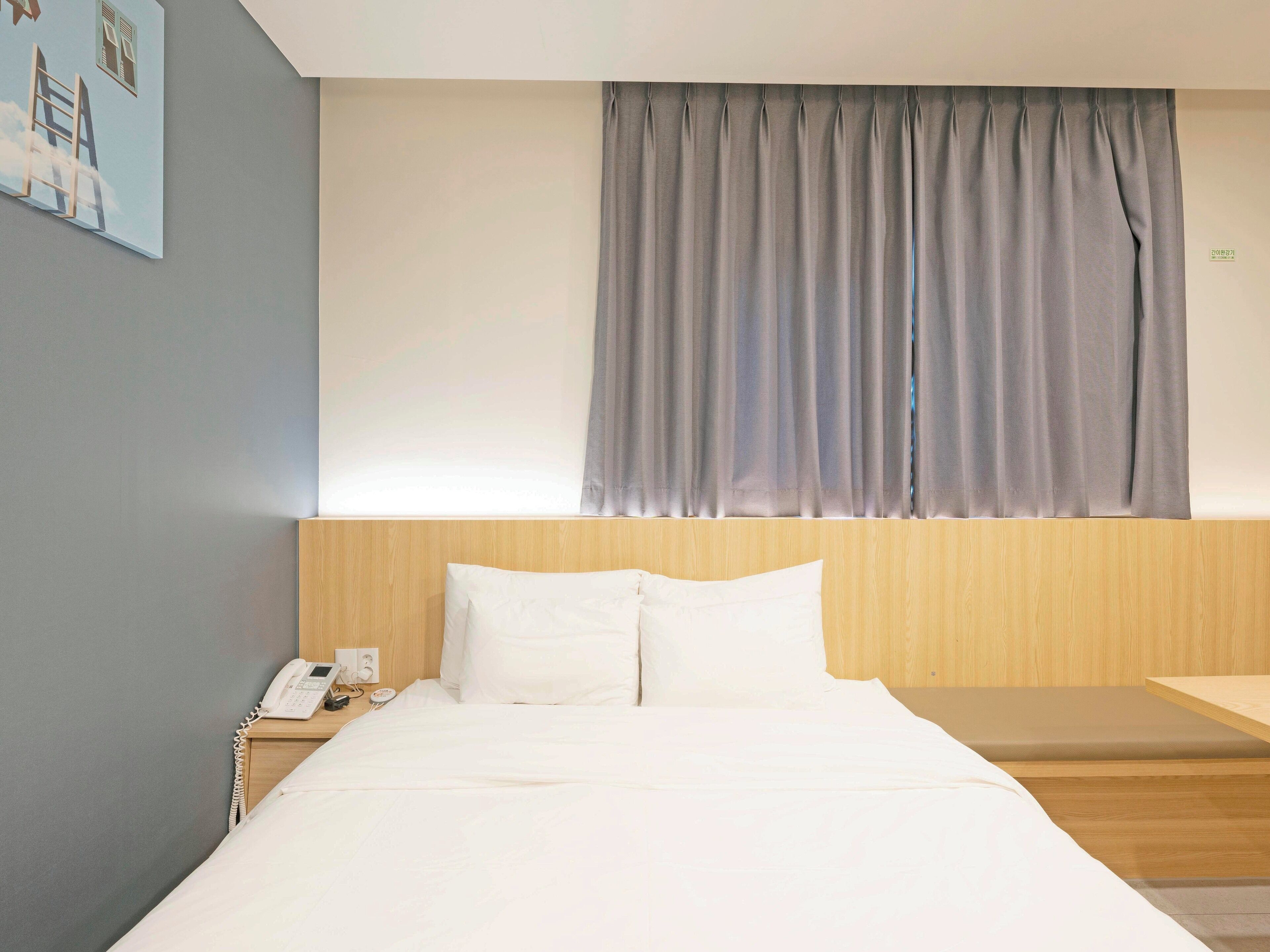 Una habitación de hotel con una cama, una mesita de noche con teléfono y una ventana con cortinas.