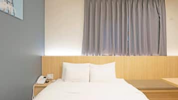 Una habitación de hotel con una cama, una mesita de noche con teléfono y una ventana con cortinas.